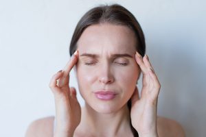 Femme yeux fermes massant ses tempes du bout des doigts, signe de tension cervicale et de cephalee.