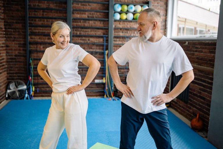 Couple de seniors mains sur les hanches en echauffement debout sur tapis bleu dans une salle d'exercices.