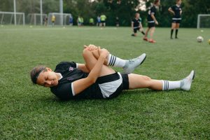 Joueuse de football allongee sur la pelouse, grimacant et serrant son genou blesse pendant l'entrainement.