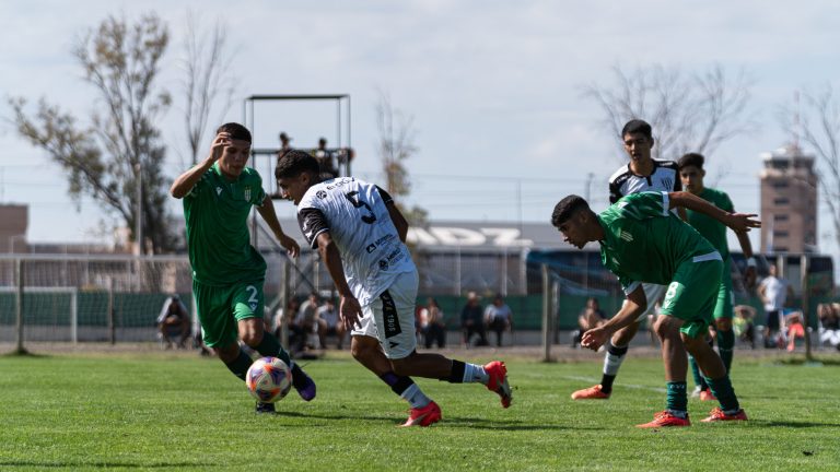 Footballeur en maillot blanc protege le ballon face a trois adversaires en vert lors d'un match sur pelouse.