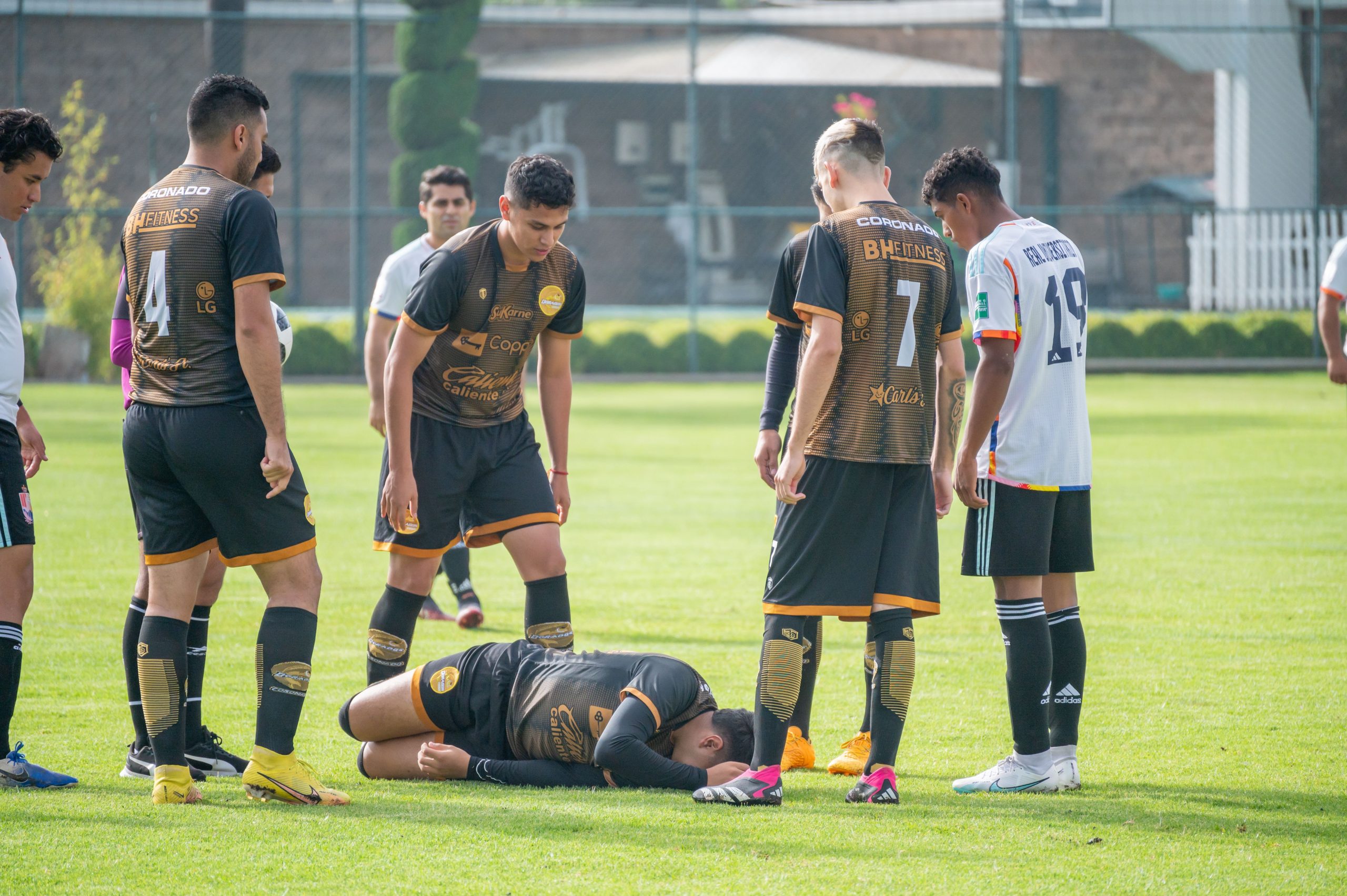 Footballeur au sol blessé sur le terrain, entouré de coéquipiers et adversaires arrêtant le jeu autour de lui.