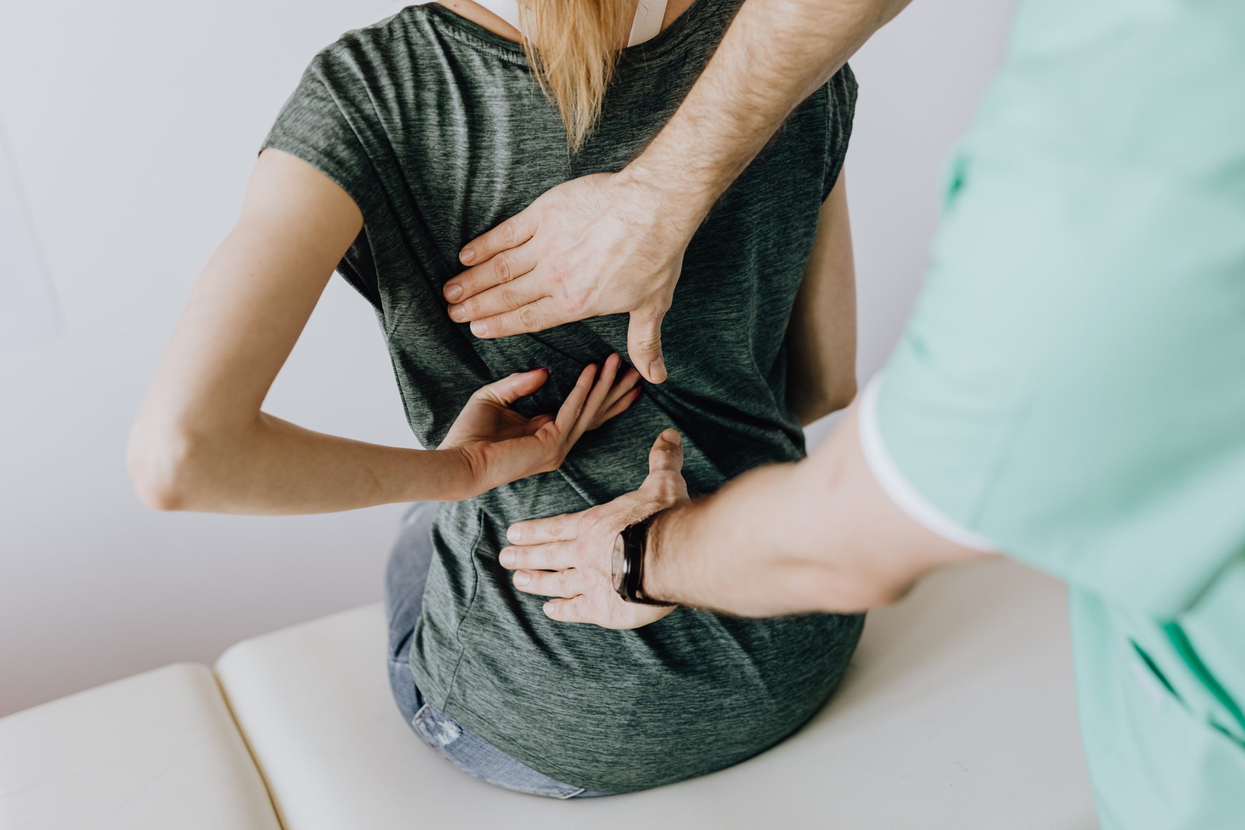 Kinesitherapeute palpant le bas du dos d'une patiente assise pour localiser une douleur sciatique lombaire.