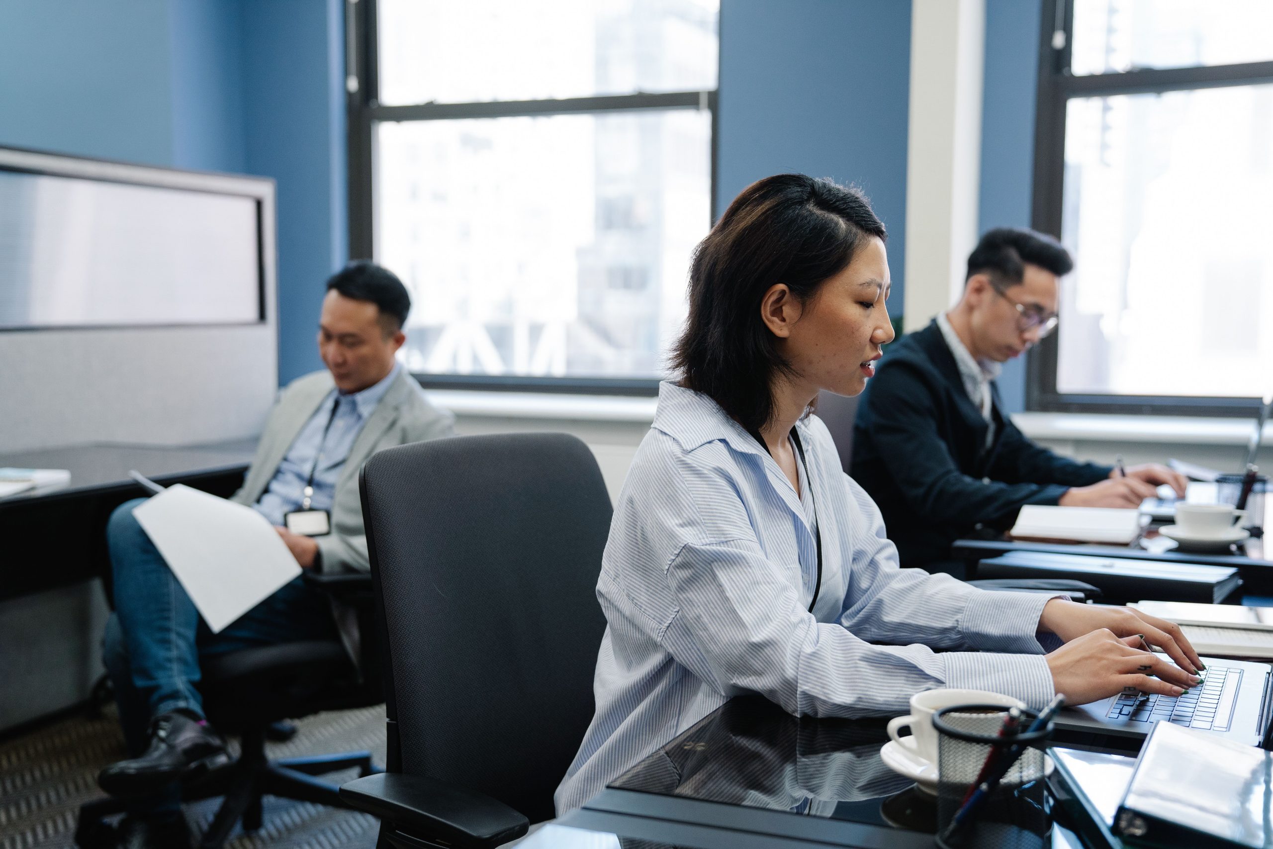 Salariee assise au bureau tapant sur un ordinateur portable, posture prolongee propice au mal de dos en open space.