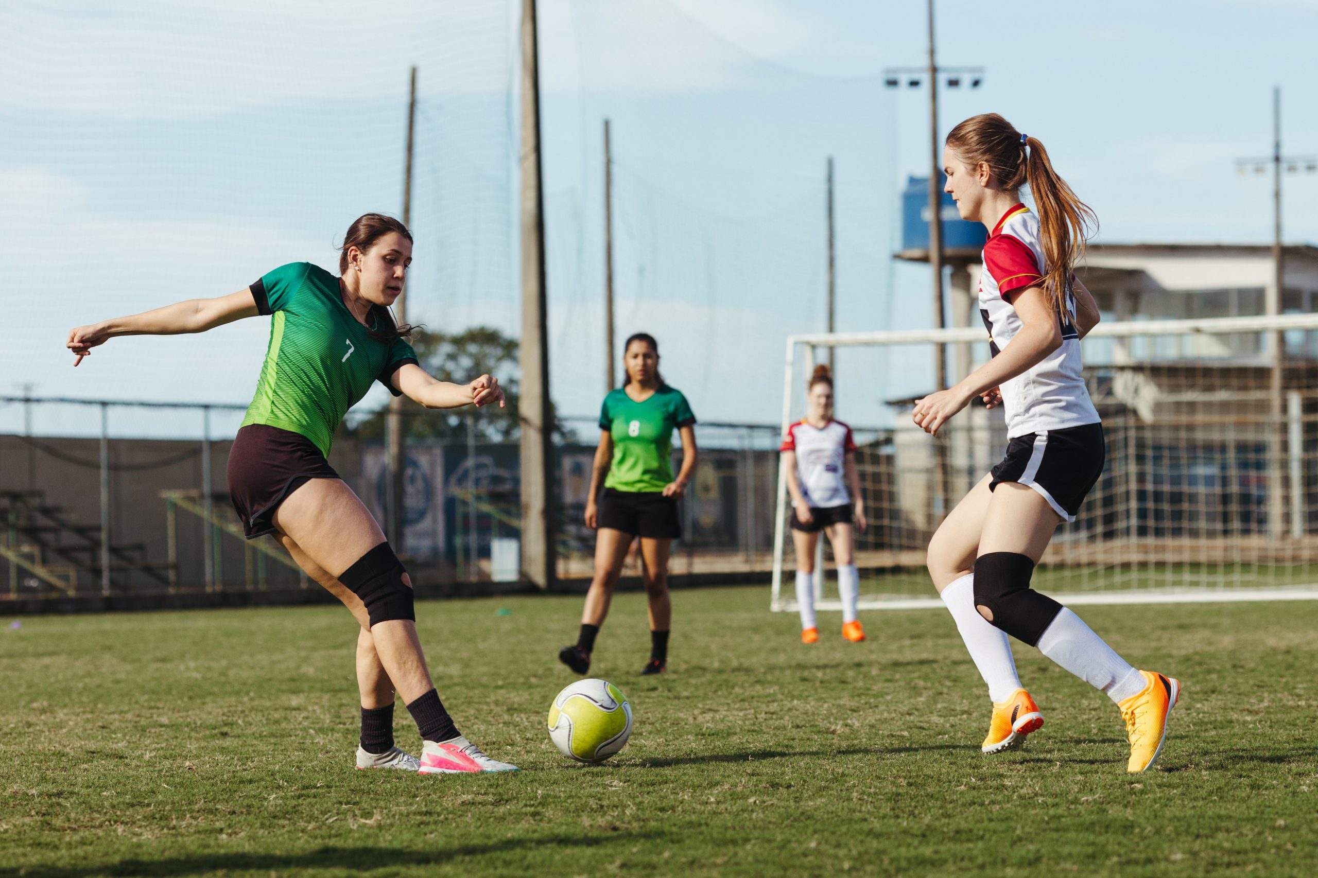 Footballeuses en duel pour le ballon sur un terrain, l'une portant une genouillere de soutien apres contracture.